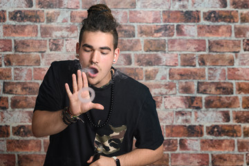 Vaper Smoke outdoor electronic cigarette near the brick wall. Young man smoking big cloud of steam