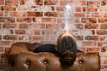 Vaper Smoke outdoor electronic cigarette near the brick wall. Young man smoking big cloud of steam