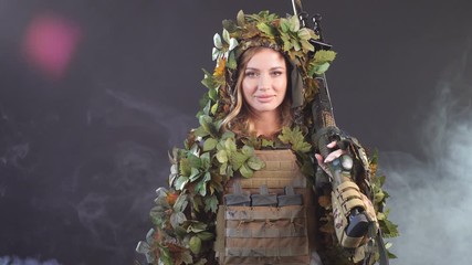 Camouflaged woman sniper in ghillie suit posing with rifle in foggy night. Special Weapons and Woman Concept.