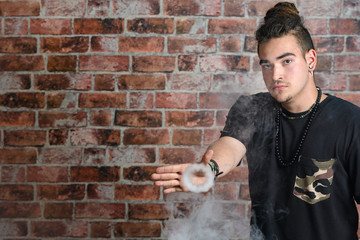 Vaper Smoke outdoor electronic cigarette near the brick wall. Young man smoking big cloud of steam