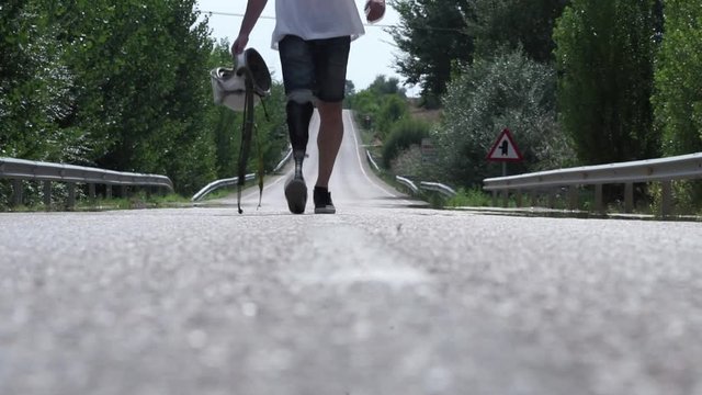 Man walking along the road with a helmet in his hand and a prothesis in his leg