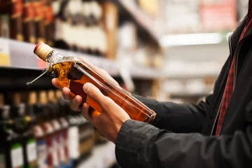 Muurstickers Een man haalt alcoholische dranken uit het schap van de supermarkt. Winkelen voor alcohol in de winkel. © Stanislaw Mikulski