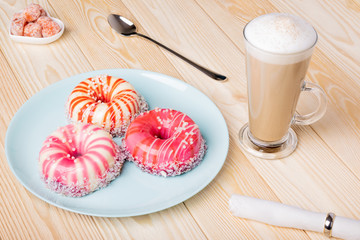 Elegant striped sponge cakes with a shiny glaze, coconut flakes and sugar pearls in the shape of a doughnut. Dried kumquat, coffee latte, long spoon, napkin
