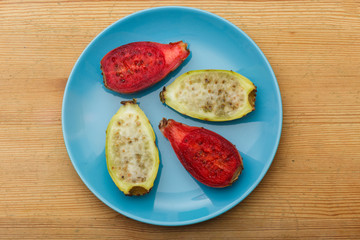 View from above of red  and yellow indian figs (also called prickly pears) on a blue plate.