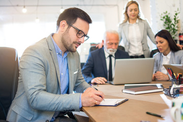 Handsome young business man writing notes on a clipboard in office