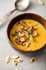 Pumpkin soup in a bowl garnished with pumpkin seed and croutons.