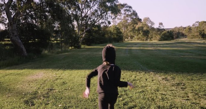 young boy wearing a homemade ninja mask and black costume practices ninja moves, ninjutsu, kicking towards the camera and moving forward one kick at a time in a park in the afternoon golden glow