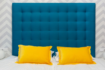Bed with upholstered blue headboard and two yellow pillows