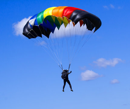 Skydiver with a very bright colorful parachute on a blue sky background.