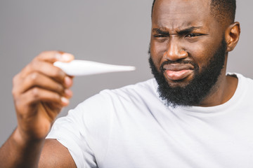 African american man standing over isolated grey background, illness and fever, flu and cold, virus sick, using thermometer.