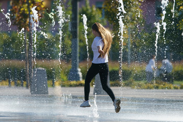 Photography of a girl playing with fountain. She jumping over water sprays. Concepts of walking, happiness, childhood and freshness in hot summer day.