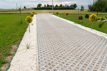 Entry for cars into the property made of openwork concrete pavement filled with colorful pebbles,...