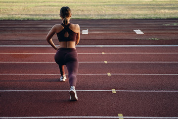 Fototapeta premium Back view of sporty girl in sportswear doing stretching exercises on stadium. Fitness woman doing warm up workout outdoor