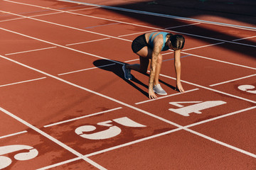 Confident athlete girl in sportswear standing in starting position ready for running on stadium