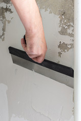 The worker covers the uneven walls, man's hands with a large spatula and putty, apartment repair