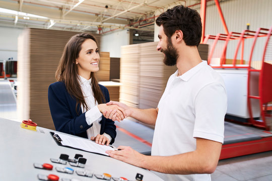 Businesswoman and employee shaking hands in a factory