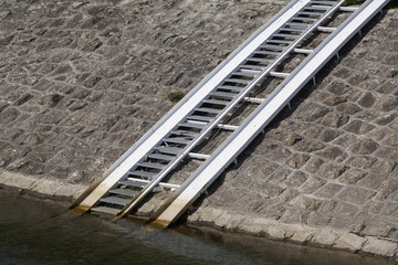 Obraz premium old iron ladder on the stone shore of the lake to lift a boat or boat ashore. traces of the level of movement of water in the lake