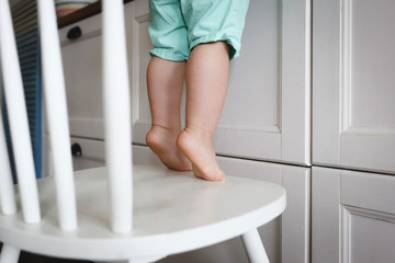 Little boy standing on tiptoes on chair in kitchen
