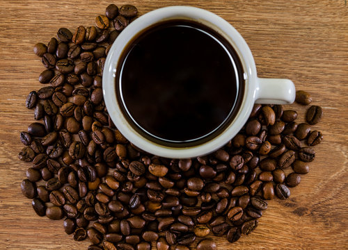 cup of coffee and a pile of coffee beans on a wooden background. Close-up. © Tania