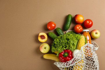 Bunch of mixed organic fruits, vegetables & greens, gourmet pile in full eco friendly shopping bag to reduce ecological footprint. Zero waste concept. Brown table background, copy space, close up.