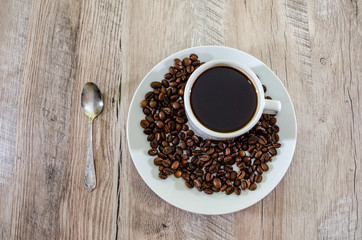 cup of black coffee, coffee beans and spoon on a wooden background.
