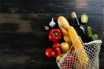 Bunch of mixed organic fruits, vegetables & greens, gourmet pile in full eco friendly shopping bag to reduce ecological footprint. Zero waste concept. Wood table background, copy space, close up.