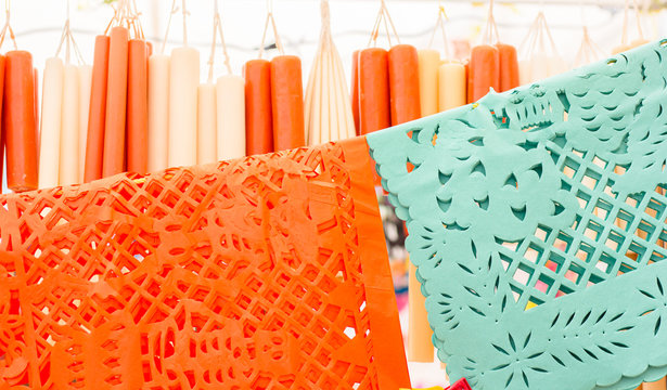 Papel d&iacute;as de muertos en m&eacute;xico, papel picado en anaranjado y aguamarina, al fondo velas para ofrenda