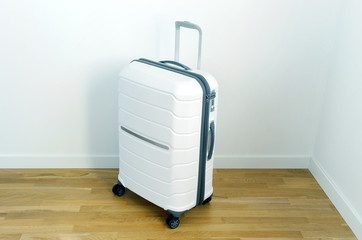White plastic suitcase or luggage for a traveler standing in the corner of the room. White suitcase isolated on white background. Polycarbonate suitcase isolated on white. 