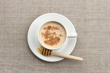 Spicy warming tea with milk in a white porcelain cup with honey and honey dipper on a textile background