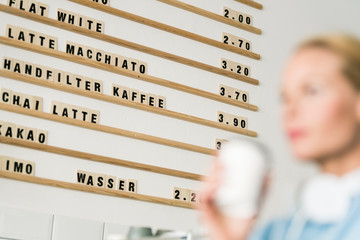 Price board in a coffee shop with customer carrying cup of coffee