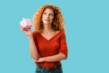 pensive redhead woman with gift box isolated on blue