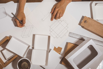 Designer draws a mockup for crafting eco cardboard box. Development a sketch of paper packaging.