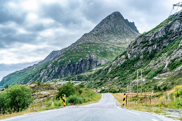 The road in Norwegian Mountais, summer day, clouds just above the tops. The power line from the right side of the road. Donna Island, Northern Norway
