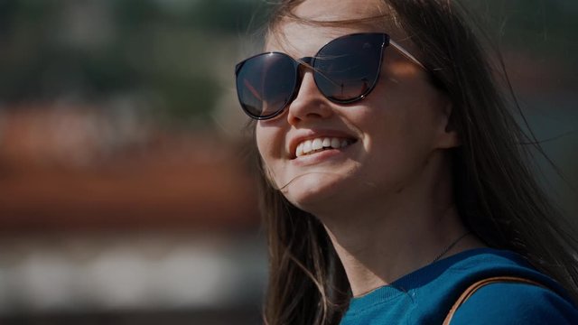 smiling girl in sunglasses adjusts her hair waving from the wind