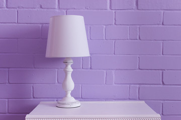 White table lamp stands on a white nightstand against a lilac wall