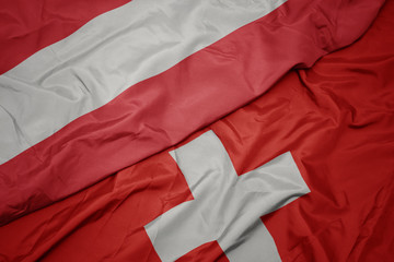 waving colorful flag of switzerland and national flag of austria.