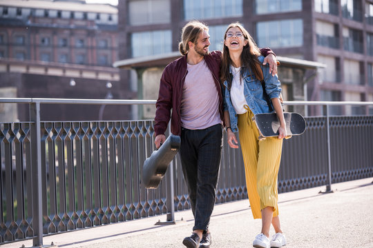 Happy young couple with skateboard walking on a bridge
