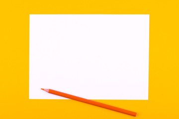 A white sheet of paper for drawings, texts and notes next to a pencil lies on an orange background