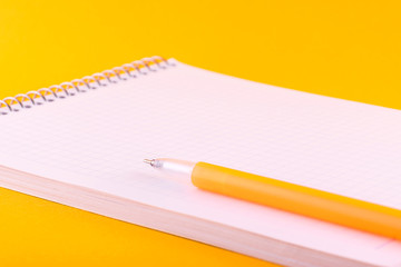 Notebook on a spring with white sheets of paper for drawings, texts and notes, next to a yellow pen lies on an orange background