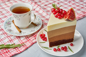 A piece of homemade cake decorated with red currants, figs, cinnamon and rosemary with a tablecloth, Cup and saucer on a light background concrete table.