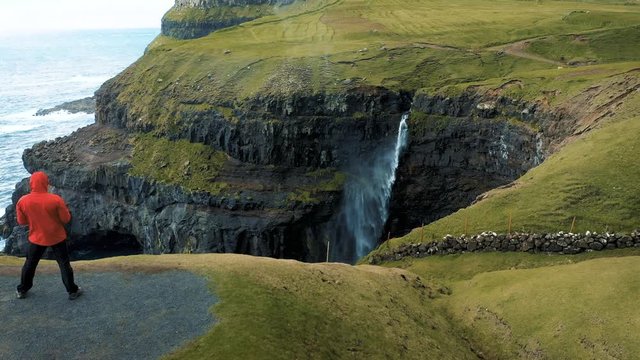 Flying around a hiker at the Gasadalur waterfall on Faroe Islands, Denmark