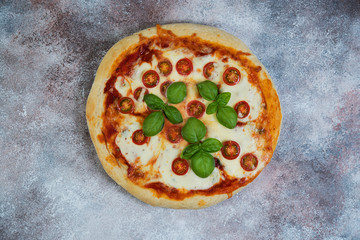Pizza Margarita with tomatoes and mozzarella cheese on a concrete background.