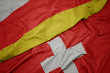 waving colorful flag of switzerland and national flag of south ossetia.