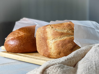 Two loaves of freshly baked bread lie on a table on a wooden board for cutting bread in paper bags. The near foreshortening.