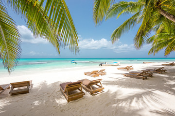Fototapeta na wymiar Chaise-longues on a beautiful white sand beach with coconut trees. Turquoise water of the Caribbean on the Saona island