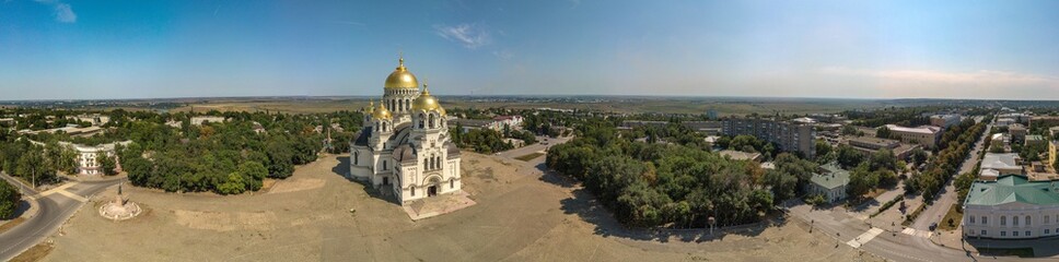 Obraz premium The Golden-domed Ascension Cathedral on Yermak Square in the provincial town of Novocherkassk in southern Russia. Luxurious aerial view on a sunny summer day mid-August.