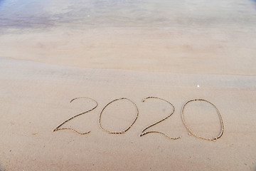 Handwritten inscription 2020 on beautiful sand beach. Lettering on beach with wave and clear blue sea. New Years 2020 concept.