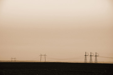 Fototapeta na wymiar Power lines on background of sky close-up. Silhouette of electric pole with copy space in sepia tones. Wires of high voltage above ground. Electricity industry in monochrome.