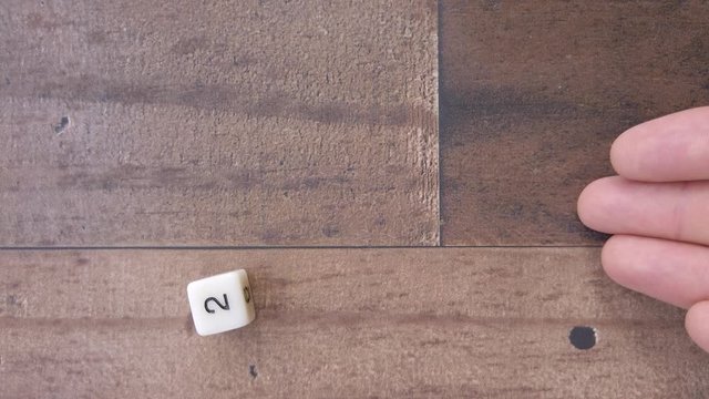 Hand rolls a 2 on a 6 sided dice. 4k, flat lay, brown wood background.