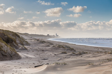 Beautiful wintry dune scenery along Dutch North Sea coast with by wind power carved deep holes with steep walls and in wind bending European Beachgrass and background sky with blue spots and clouds - obrazy, fototapety, plakaty